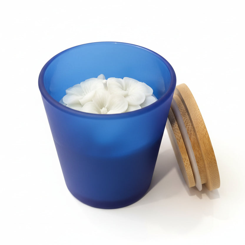 Blue glass candle with white floral wax design and bamboo lid on white background