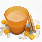 Scented candle in orange glass jar with bamboo lid, surrounded by coconut and mango pieces