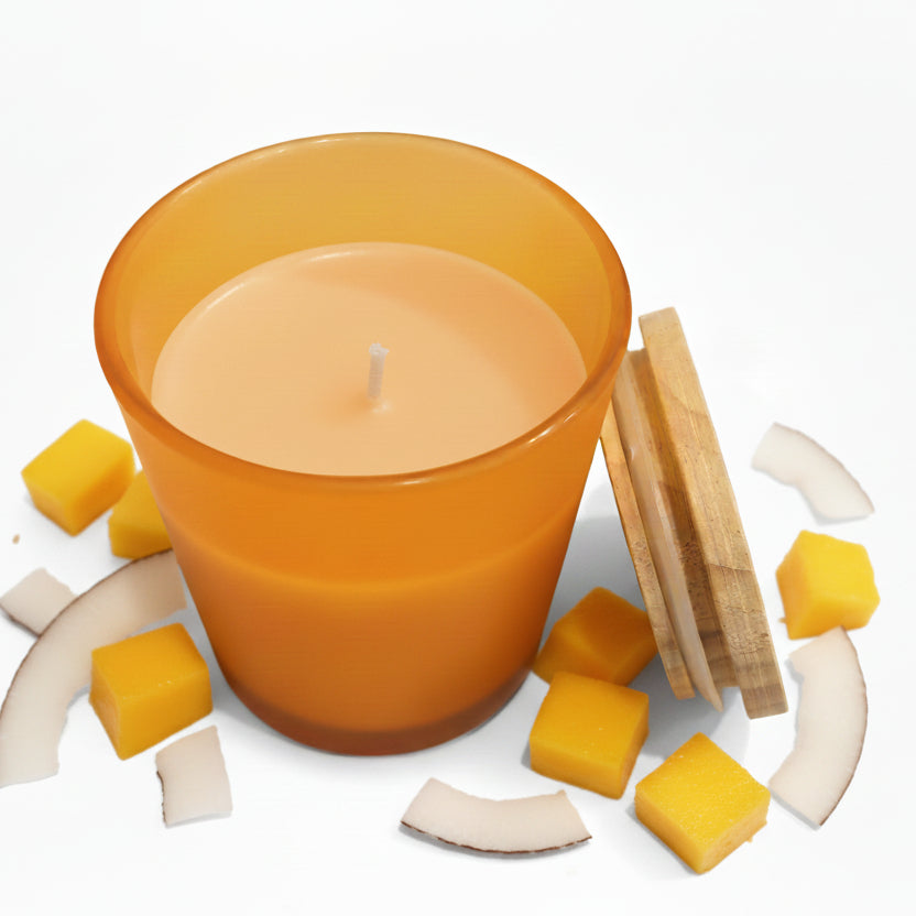 Scented candle in orange glass jar with bamboo lid, surrounded by coconut and mango pieces