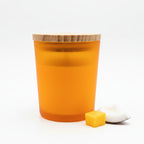 Amber frosted glass candle with wooden lid, mango cube and coconut pieces on white background