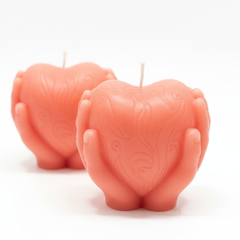 Two sculptural heart-shaped candles held by hands, natural wax, decorative carved design.