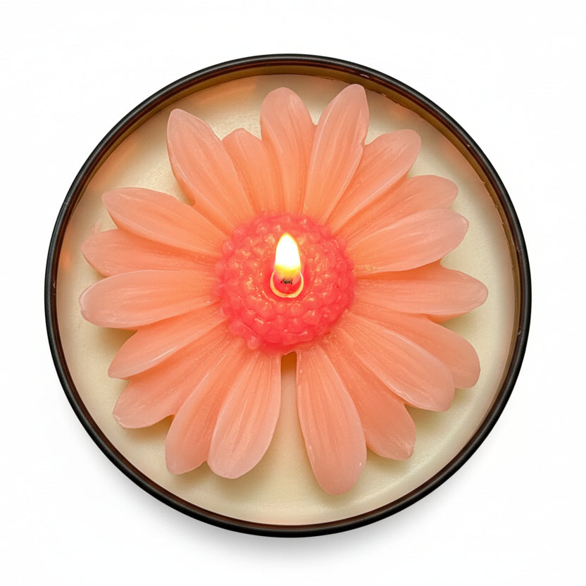 Pink flower-shaped sculptural candle in a round container, lit, on white background