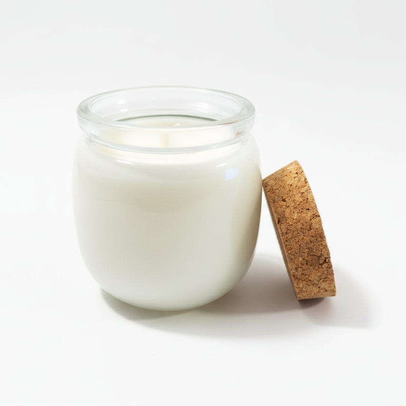 Coconut wax candle in a clear glass jar with cork lid on white background